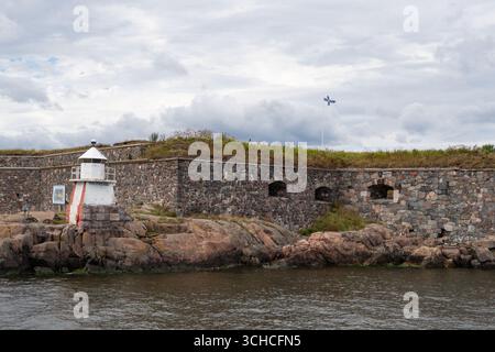 Historische Festungsmauer mit Leuchtturm an der felsigen Ostseeküste unter bewölktem Himmel Stockfoto