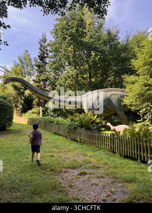 Rückansicht eines Jungen, der zu einer großen Dinosaurierfiguren-Statue läuft, im Vergnügungspark für Kinder Stockfoto