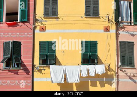 265 Orange, Gelb und Rosa Fassaden mit grünen Fensterläden von Gebäuden auf der Piazza Guglielmo Marconi, Wäschetrocknung in der Sonne. Vernazza-Italien. Stockfoto
