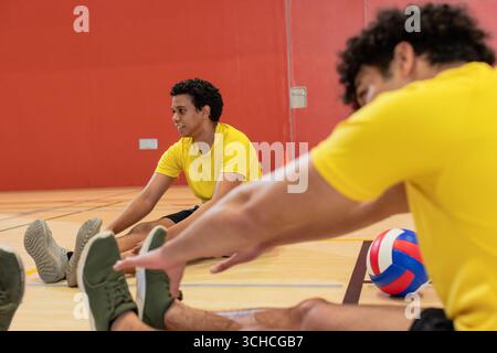 Afroamerikanische Teamkollegen, die ihre Beine auf dem Fitnessboden mit Volleyball, Kegeln und Kopierraum Strecken. Athleten, Fitness, Training, Sport, Wellness, Teamwork, dy Stockfoto