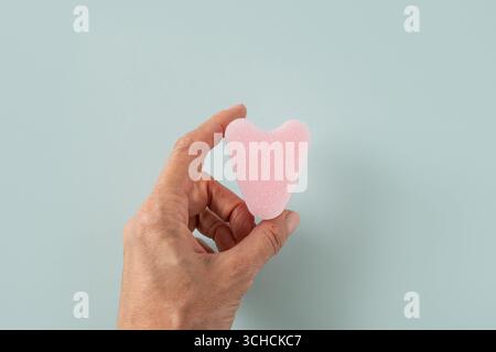 Rosa hygienischer stringloser Tampon als Herz in der Frauenhand auf blauem Hintergrund. Hygienezubehör für Frauen. Blick von oben. Stockfoto