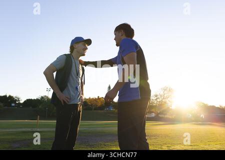 Männlicher Trainer und Athlet, der bei Sonnenuntergang auf dem Feld steht, mit Mütze und Whistle-Lanyard, Blickmarker. Coaching, Mentoring, Leichtathletik, Teamwork, Outdo Stockfoto