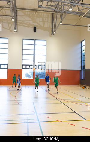 Verschiedene männliche Basketballspieler, die Trikots tragen, laufen auf dem Sportplatz auf den Basketball zu. Athleten, Teamwork, Wettkampf, Energie, Vibrant, Stockfoto