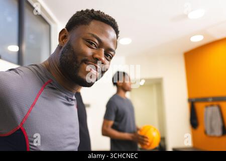 Afroamerikanische männliche Freunde lächeln in die Kamera und halten Basketball in der Umkleidekabine, Kopierraum. Athletik, Kameradschaft, Teamwork, Fitness, Sportbekleidung, Stockfoto