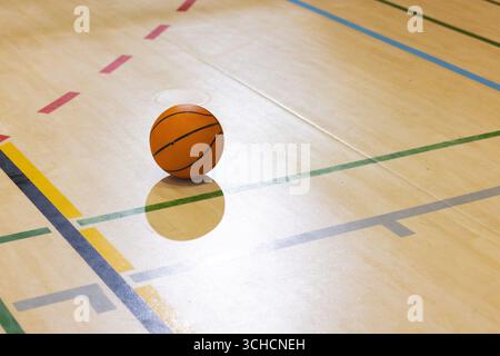 Orangefarbener Basketball auf poliertem Hallenboden mit grünen gelben dunkelblauen und roten Feldlinien. Sportlich, Sport, Training, Fitness, lebendig, Mitbewerber Stockfoto