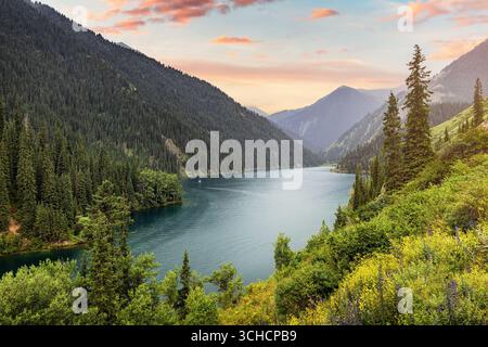 Wunderbarer Sonnenuntergang über dem Kolsai Bergsee in Kasachstan mit farbenfrohem Himmel, der sich in türkisfarbenem Wasser spiegelt Stockfoto