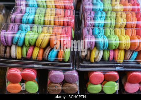 Verschiedene Regenbogenmakaronen in einer durchsichtigen Kunststoffbox. Helles und farbenfrohes Dessert mit glatter Textur und süßer cremiger Füllung. Stockfoto