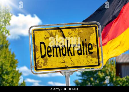 Deutschland - 31. August 2025: Eine Fotomontage, Ein verwittertes Schild mit der Aufschrift Demokratie vor der deutschen Flagge, symbolisiert die Bedrohung für Freiheit, Rechtsstaatlichkeit und Grundrechte durch wachsende Krisen und politischen Extremismus. *** Fotomontage, ein verwittertes Schild mit der Aufschrift Demokratie vor deutscher Flagge symbolisiert die Gefahr für Freiheit, Rechtsstaat und Grundrechte durch wachsende Krisen und politischen Extremismus. Stockfoto