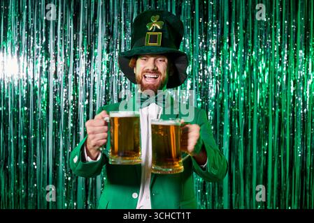 Junger Ginger-Mann, gekleidet als Kobold, der zwei Bierbecher hält Stockfoto