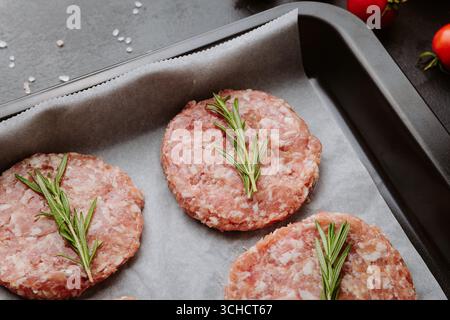 Vier rohe Schweinebraten mit Rosmarin zum Grillen, Blick von oben mit Zutaten Stockfoto