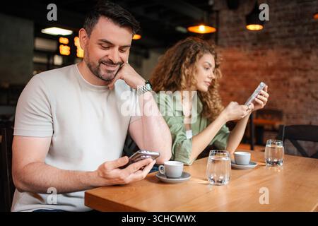 Ein junges Paar, das auf ihre Smartphones schaut, während er an der Bar Kaffee trinkt Stockfoto