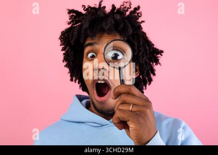 Schockiert schwarz teen Kerl suchen durch Lupe auf rosa Studio Hintergrund. Geheimnis, Zweifel Konzept Stockfoto