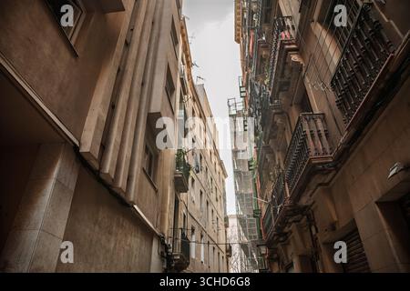 Enge Straße in Ciutat Vella, Barcelona, gesäumt von alten Apartmentblöcken, Balkonen, Wäscherei und Gerüsten. Die schmale Perspektive zeigt ein dichtes hous Stockfoto
