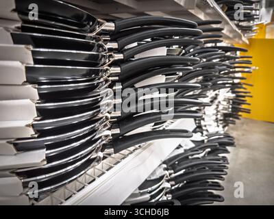 Reihen antihaftbeschichteter Pfannkuchenpfannen mit langen schwarzen Griffen, die auf Regalen in Supermärkten angeordnet sind. Die Perspektive zeigt ein Kochgeschirr-Display, das Teflon c hervorhebt Stockfoto