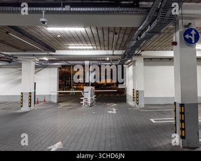 Nachtblick in einer Tiefgarage mit Schranke, Ticketautomat und CCTV unter Leuchtstofflampen. Leere Gassen, Pfeile und Betonpfosten Stockfoto