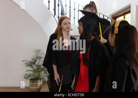 Absolventen in Mützen und Kleidern feiern gemeinsam zu Hause. Abschluss, Feier, Leistung, Freude, Leistung, Erfolg Stockfoto