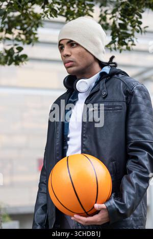 afroamerikaner, der draußen vor der Wand steht und Basketball hält, mit Kopfhörern Stockfoto