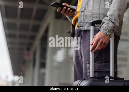afroamerikaner wartet auf Bahnsteig mit Smartphone und Ziehkoffer Stockfoto
