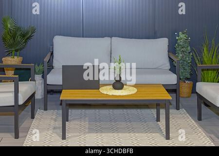 Hölzerner Kaffeetisch vor dem grauen Sofa auf der Terrasse Stockfoto
