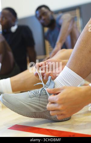 Asiatischer Mann in Shorts, der Laufschuhe auf dem Hallenboden neben der roten Linie unter den Trainingsstäben bindet Stockfoto