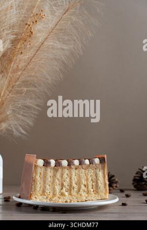 Ein wunderschön präsentiertes Stück Kuchen mit Schichten Sahne und Schwamm, dekoriert mit Schokolade und Cremebällchen, vor einer rustikalen Kulisse Stockfoto