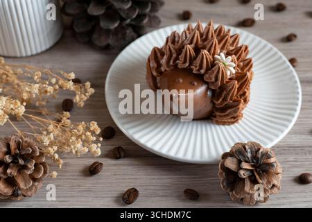Ein dekadentes Schokoladendessert auf einem weißen Teller, umgeben von Kaffeebohnen, Tannenzapfen und getrockneten Blumen auf einer Holzoberfläche, die einen gemütlichen Herbst schafft Stockfoto