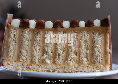 Nahaufnahme einer geschichteten Biskuitscheibe mit Sahneschichten, gekrönt mit Schokolade und Vanilleperlen. Ideal für Food Blogs, Menüs und kulinarische Geschenke Stockfoto