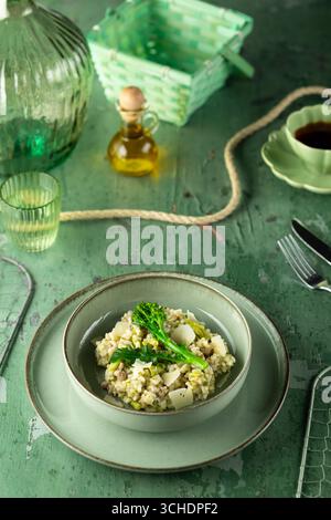 Cremiges Risotto mit Brokkoli, Erbsen, Parmesan, serviert in einer grünen Schüssel auf grünem Tisch, bereit zum Genießen Stockfoto