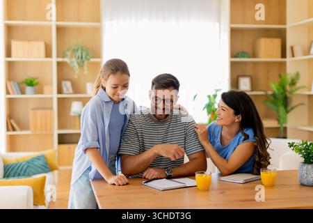 Eine fröhliche Familie genießt zu Hause eine gute gemeinsame Zeit, während sie Lachen und Ideen teilt, während sie Saft schlürft und Notizen schreibt. Stockfoto