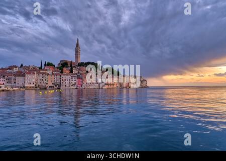 Häuser in der Küstenstadt Rovinj und der Glockenturm der Kirche St. Euphemia, die bei Sonnenuntergang über dem Wasser des Mittelmeers zu sehen sind. Stockfoto