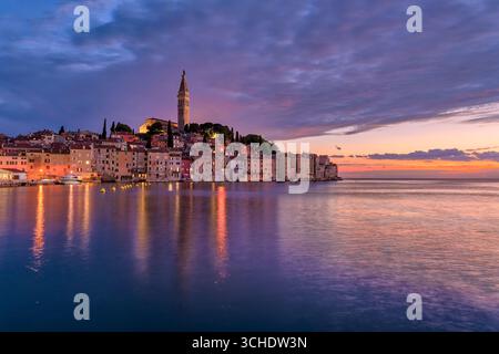 Häuser in der Küstenstadt Rovinj und der Glockenturm der Kirche St. Euphemia, die bei Sonnenuntergang über dem Wasser des Mittelmeers zu sehen sind. Stockfoto