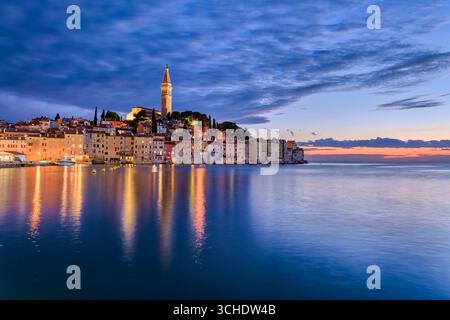 Häuser in der Küstenstadt Rovinj und der Glockenturm der Kirche St. Euphemia, die bei Sonnenuntergang über dem Wasser des Mittelmeers zu sehen sind. Stockfoto