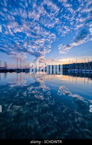 Die untergehende Sonne, farbenfrohe Wolken und Segelboote spiegeln sich im Wasser des Yachthafens von Castelreggio wider. Stockfoto