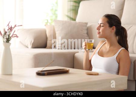 Eine entspannte Frau riecht Weihrauch und trinkt Tee im Wohnzimmer zu Hause Stockfoto