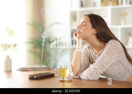 Frau, die zu Hause Räucherstäbchen auf einem Holztisch riecht Stockfoto