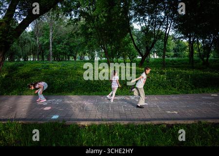 Kinder genießen bei sonnigem Wetter in einem üppig grünen Park die Kreidezeichnungen von Hopscotch. Stockfoto