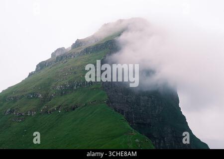 Ein atemberaubender Berg erhebt sich dramatisch aus der üppigen grünen Landschaft der Färöer, teilweise von sanftem Nebel verdeckt. Kallur Lighthouse, Kalsoy Island Stockfoto
