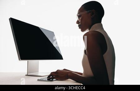 Eine professionelle Frau, die auf einem schlanken Computer schreibt, beleuchtet vor weißem Hintergrund. Präsentiert moderne Technologie, Unternehmenseffizienz und Fokus i Stockfoto