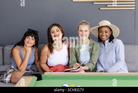 Verschiedene Gruppen von verschiedenen weiblichen Freunden sitzen auf der Couch, lächeln und genießen die Freizeit zu Hause Stockfoto