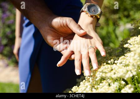 Ein Paar hält Hände im Freien und zeigt Verlobungsringe im sonnigen Garten Stockfoto