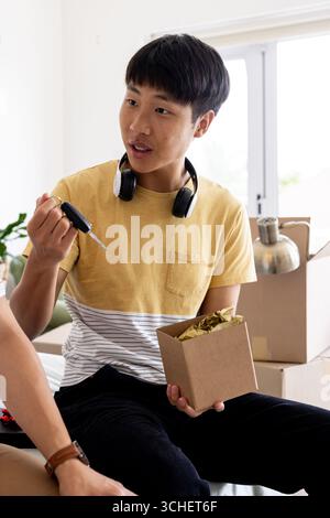 Asiatischer Mann, der Kisten auspackt, Autoschlüssel hält und zu Hause überrascht aussieht Stockfoto