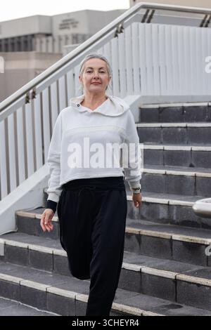Eine ältere Frau, die die Außentreppe entlang neben dem Handlauf hinuntergeht und Smartwatch überprüft Stockfoto