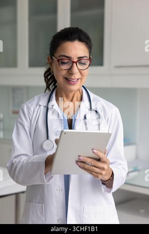Lächelnde Ärztin mittleren Alters, die am Tablet-Gerät arbeitet Stockfoto