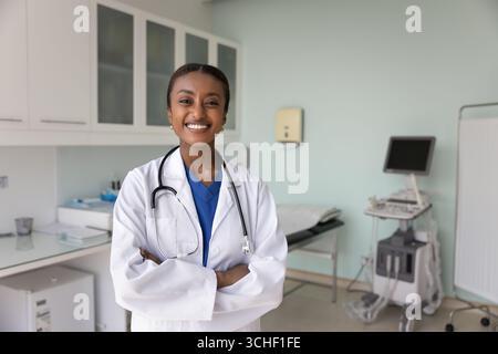 Afrikanische Ärztin in Uniform steht selbstbewusst im Sprechzimmer Stockfoto