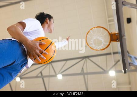 Asiatischer Mann, der Basketball hält, zielte auf den Basketball auf dem Platz unter hellem Licht, Kopierraum Stockfoto