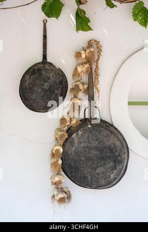 Vintage Bratpfanne und Bündel von Knoblauch auf eine weiße Wand, aus der Nähe. Die Insel Kos, Griechenland Stockfoto