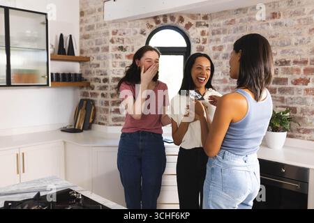 Lachen und reden, vielfältige Freundinnen in der modernen Küche, die Spaß miteinander haben, zu Hause Stockfoto