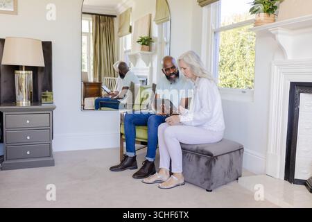 Interagierende ältere Ehepaare mit Tablet im Wohnzimmer, mit Kamin und Wandspiegel Stockfoto