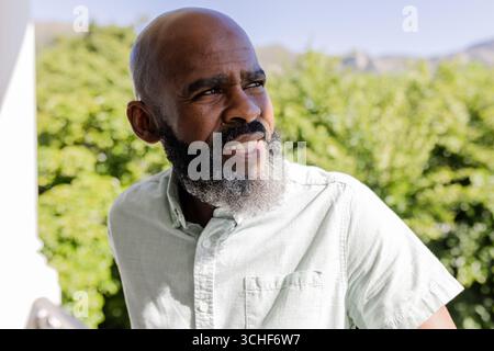 Matiure afroamerikaner steht draußen auf Balkon und beobachtet ferne Hügel hinter Hecke Stockfoto