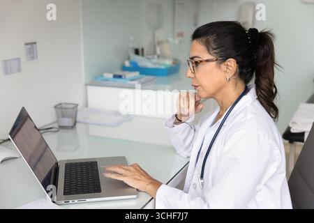 Arzt sitzt am Schreibtisch und arbeitet an einem Laptop Stockfoto